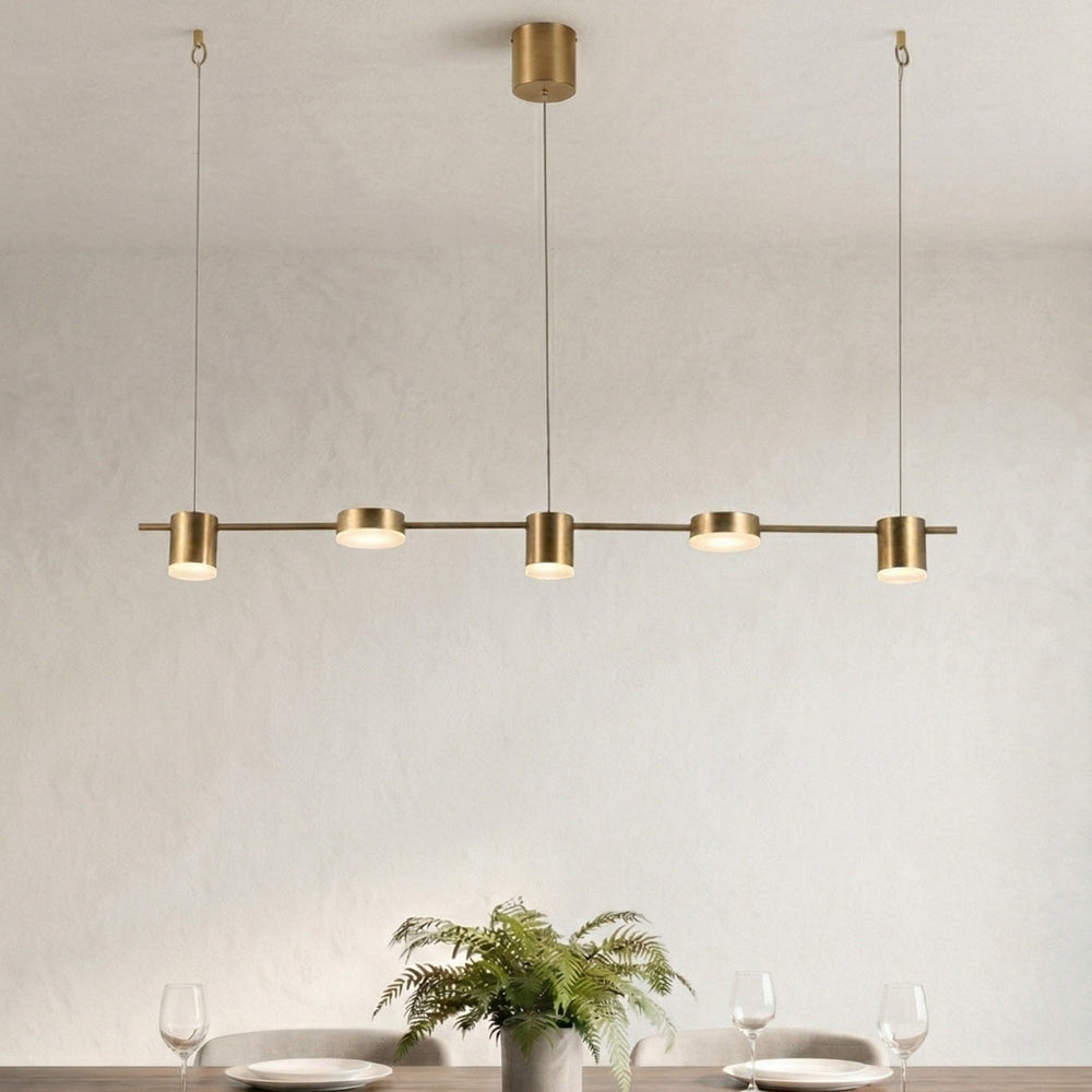 Modern gold pendant light fixture over a dining table with decor items.