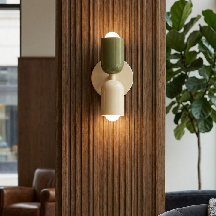 Modern wall sconce with green and white design in a room with a plant and books.