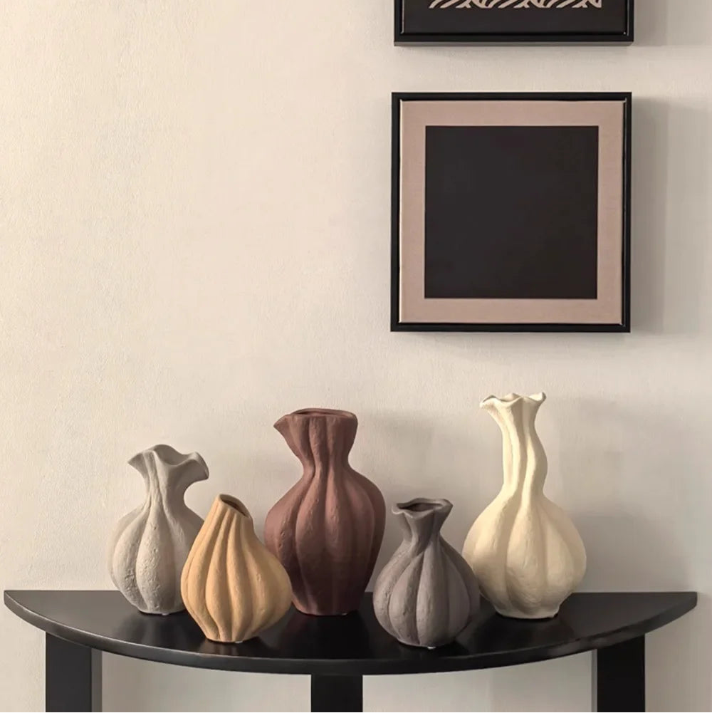 Set of five ceramic vases on a dark wooden shelf against a light wall with two framed pictures.