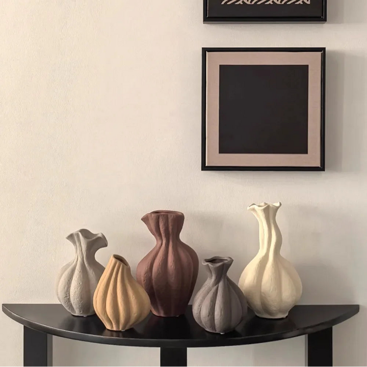 Set of five ceramic vases on a dark wooden shelf against a light wall with two framed pictures.